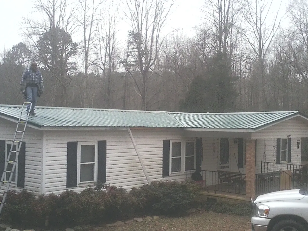Worker on a ladder beside a new green metal roof on a ranch home in George