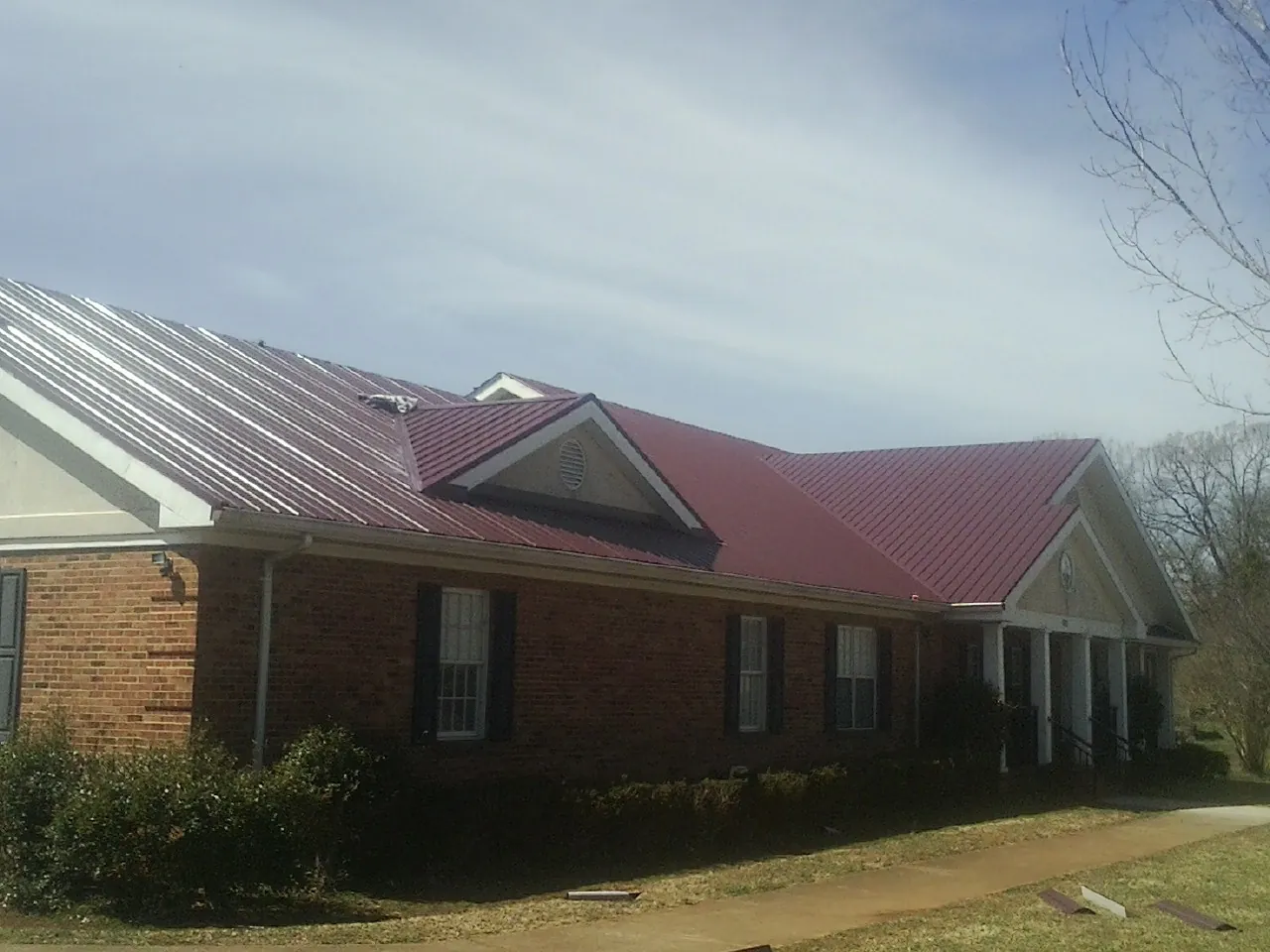 Red metal roof with gabled entries on a long brick building, from a Hail Damage Roof Repair job in George