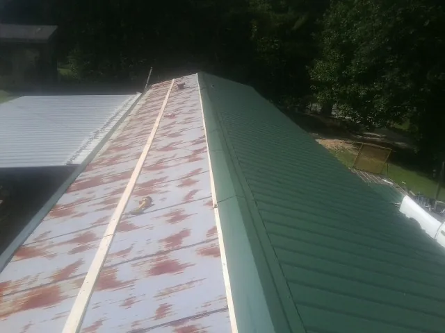 Old rusted panels beside newly installed green metal roofing — Wind Damage Roof Repair by Roofing Brothers in George