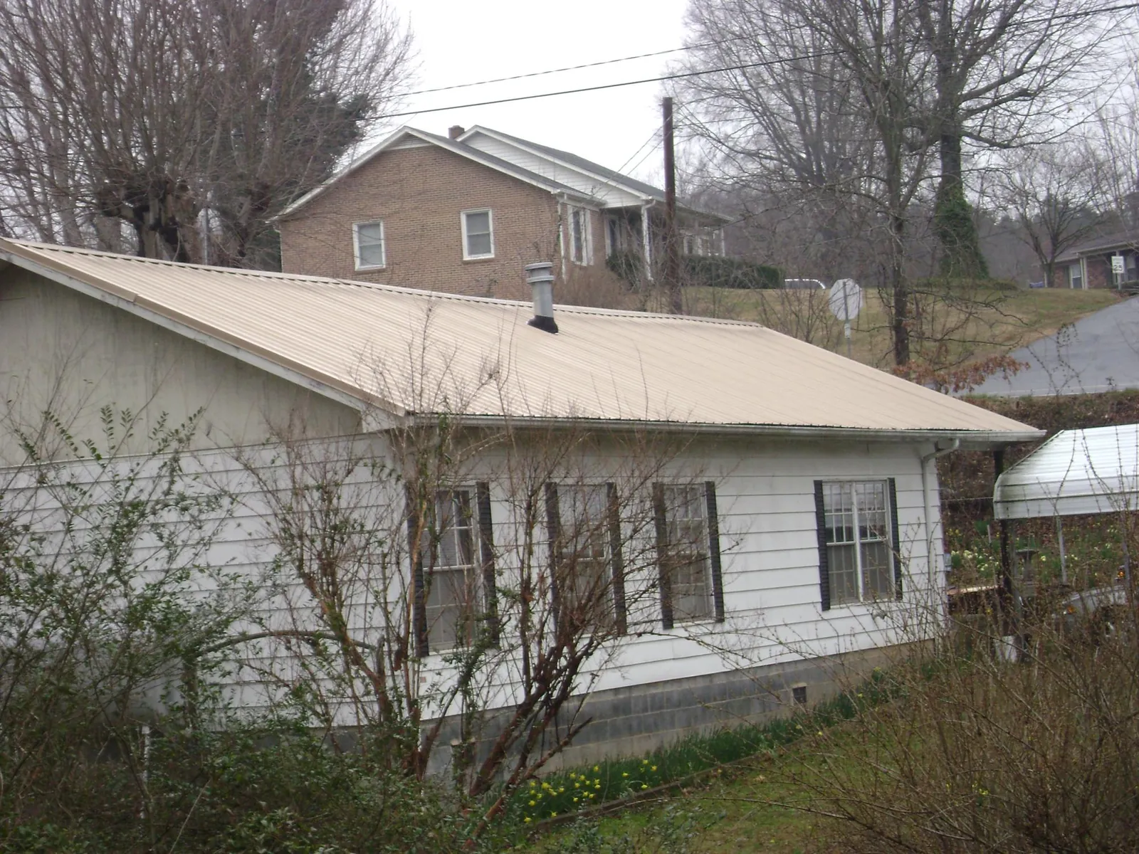 Tan metal roof on a white sided house set into a hillside — Commercial Roofing by Roofing Brothers in George